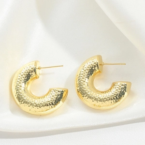 Close-up of golden C-shaped hoop earrings with hammered texture on white silk fabric