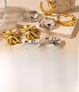 Close-up of geometric pleated C-shaped earrings and square studs in gold and steel finishes