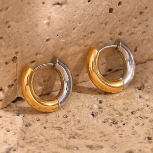 Macro view of C-shaped two-tone gold and silver stainless steel earrings on beige stone