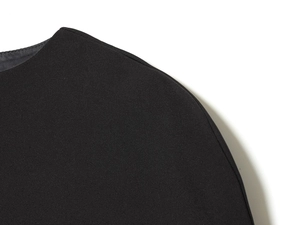 Détail de l'épaule d'une robe noire montrant la texture fine du tissu tissé et la finition