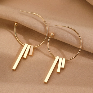 Minimalist gold geometric drop earrings with long metal bars on camel fabric background