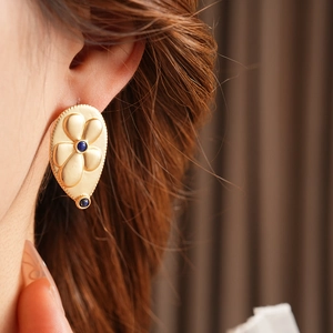Close-up of vintage teardrop gold earrings with blue gemstones and floral engraving