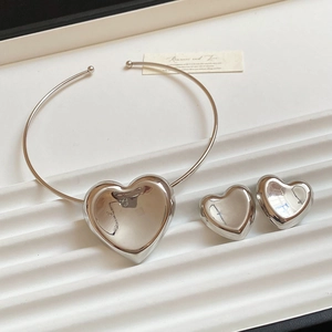 Polished silver heart pendant necklace and stud earrings set on a white textured tray