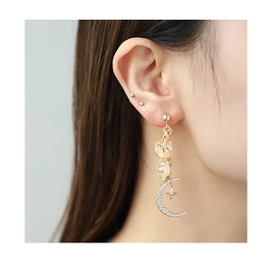 Close-up of gold drop earrings with sun, moon, and star charms set with sparkling crystals