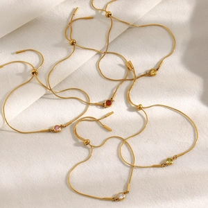 Détail de chaînes serpent dorées ajustables avec zircons colorés sur tissu blanc
