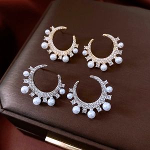Macro detail of crescent zircon and pearl earrings in gold and silver finishes