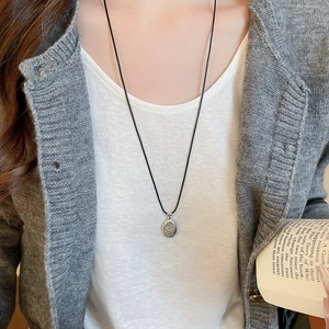 Detail of silver spiral disk pendant with black rope necklace on a model's neck