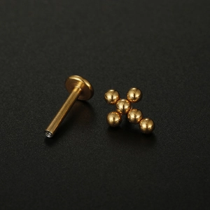 Piercing lèvre croix doré en acier inoxydable avec boules sur fond noir élégant
