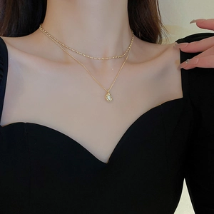 Close-up of double-layer gold necklace featuring small metal beads and a white baroque pearl