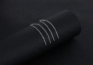 Macro detail of minimalist S925 silver long tassel earrings on a sleek black background