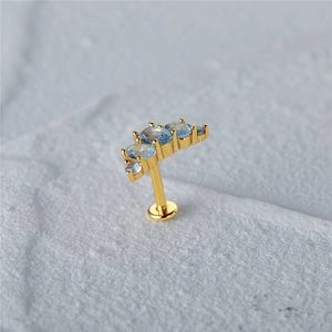 Macro shot of gold ear cartilage stud with five graduated light blue zircons on grey stone