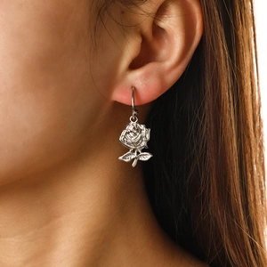 Close-up of a silver rose-shaped dangle earring with detailed texture worn by a model