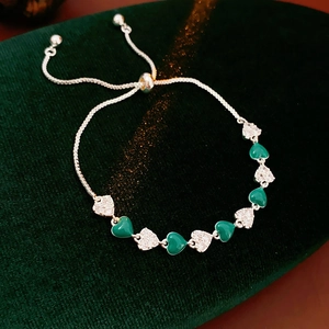 Detail of silver heart bracelet with green zircons on dark green velvet background