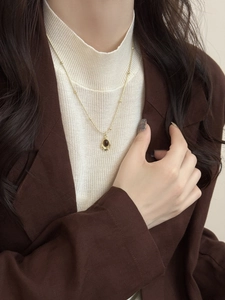 Détail d'un collier vintage doré avec gemme brune sur col roulé blanc et blazer chic
