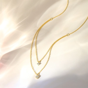 Detail of double-layer gold necklace featuring sparkling clover pendants on silk fabric