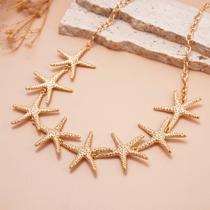 Close-up of gold starfish pendant necklace on textured stone with floral accents