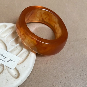 Detail of amber resin wide bangle with flowing texture on a white ceramic plate