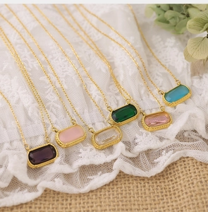 Detailed close-up of multi-colored rectangular gemstone pendants on gold chains over lace