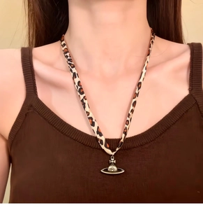 Detailed view of leopard print fabric necklace with a silver Saturn orbit pendant charm