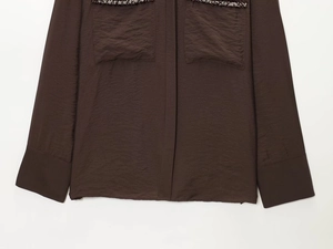 Detail of dark brown satin shirt featuring large front pockets and decorative trim textures