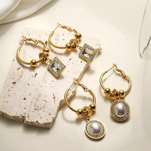 Gold geometric earrings with zircon and pearl charms on a beige stone slab