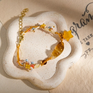 Detail of woven beaded bracelet with resin cat and star charms on ceramic tray