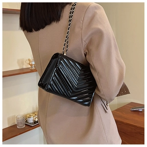 Close-up of black patent leather crossbody bag with V-shaped quilting and gold chain strap