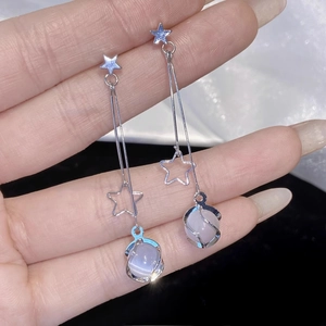Détails macro des boucles d'oreilles à pompon argenté avec étoile et pierre œil de chat