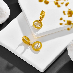Close-up of golden hoop earrings with round pendants on minimalist stone background