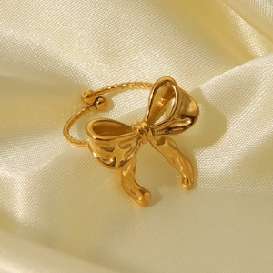 Macro shot of a golden bow-shaped open ring on silk, showing the polished metallic finish