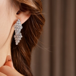 Close-up of dangling silver rhombus earrings with cubic zirconia on model's ear