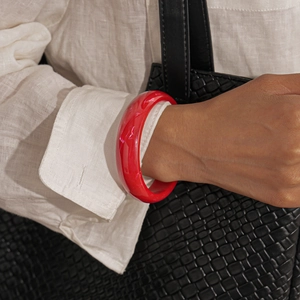 Detail of red marble texture resin bangle paired with white linen shirt and black leather bag