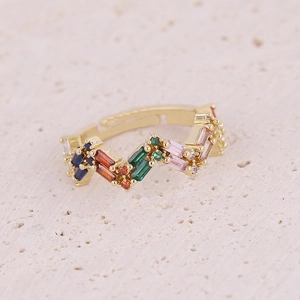 Close-up of wavy gold ring with colorful rectangle zircons on stone background