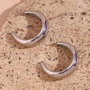 Macro detail of chunky silver stainless steel C-shape earrings on a natural stone base