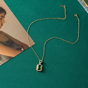 Detailed close-up of emerald square pendant necklace with gold chain on dark green base