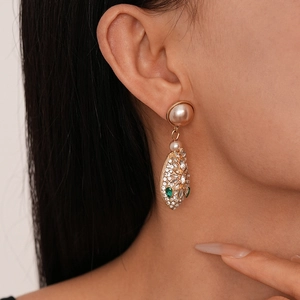 Close-up of luxury snake-shaped earring with dangling pearl and sparkling rhinestones