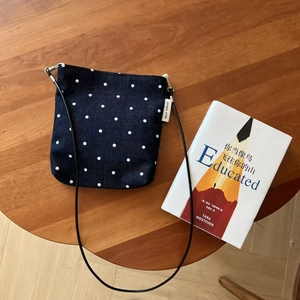 Overhead view of a blue polka dot denim crossbody bag on a wooden table with a book