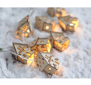 Detail of wooden mini house LED string lights with warm star cutouts on snow background