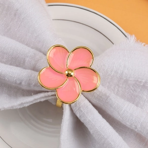 Pink metal five-petal flower napkin ring with gold edges on white linen napkin