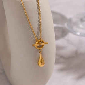 Macro view of gold teardrop pendant with toggle clasp on a minimalist display