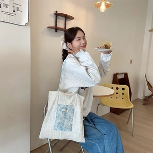 Detailed view of canvas tote bag featuring floral patch, lace trim and blue cord handle