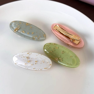 Set of four colorful oval hair clips with gold foil flakes on a white plate