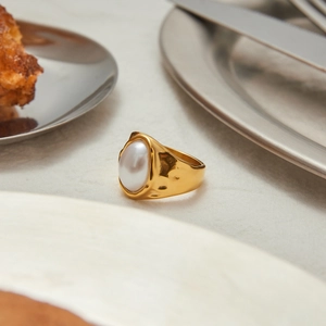Detailed view of gold hammered texture ring with an oval pearl on a stone surface