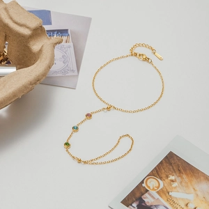Detailed macro shot of gold stainless steel hand chain with pink, blue and green gemstones