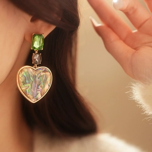 Detail of vintage heart drop earring with green stone and iridescent shell on model