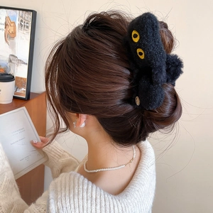 Détail d'une pince à cheveux chat en peluche noire portée dans un cadre domestique cosy