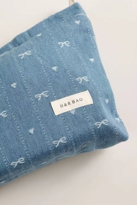 Detail of blue denim cosmetic bag with white bow embroidery and H&R BAG logo