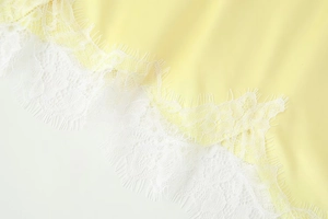 Detail of pale yellow satin fabric with delicate white eyelash lace trim on the edge