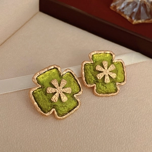 Détail de boucles d'oreilles vintage vertes avec bord doré sur cuir beige texturé
