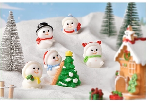 Macro shot of 5 cute snowman figurines, a Christmas tree, and gingerbread house in snow